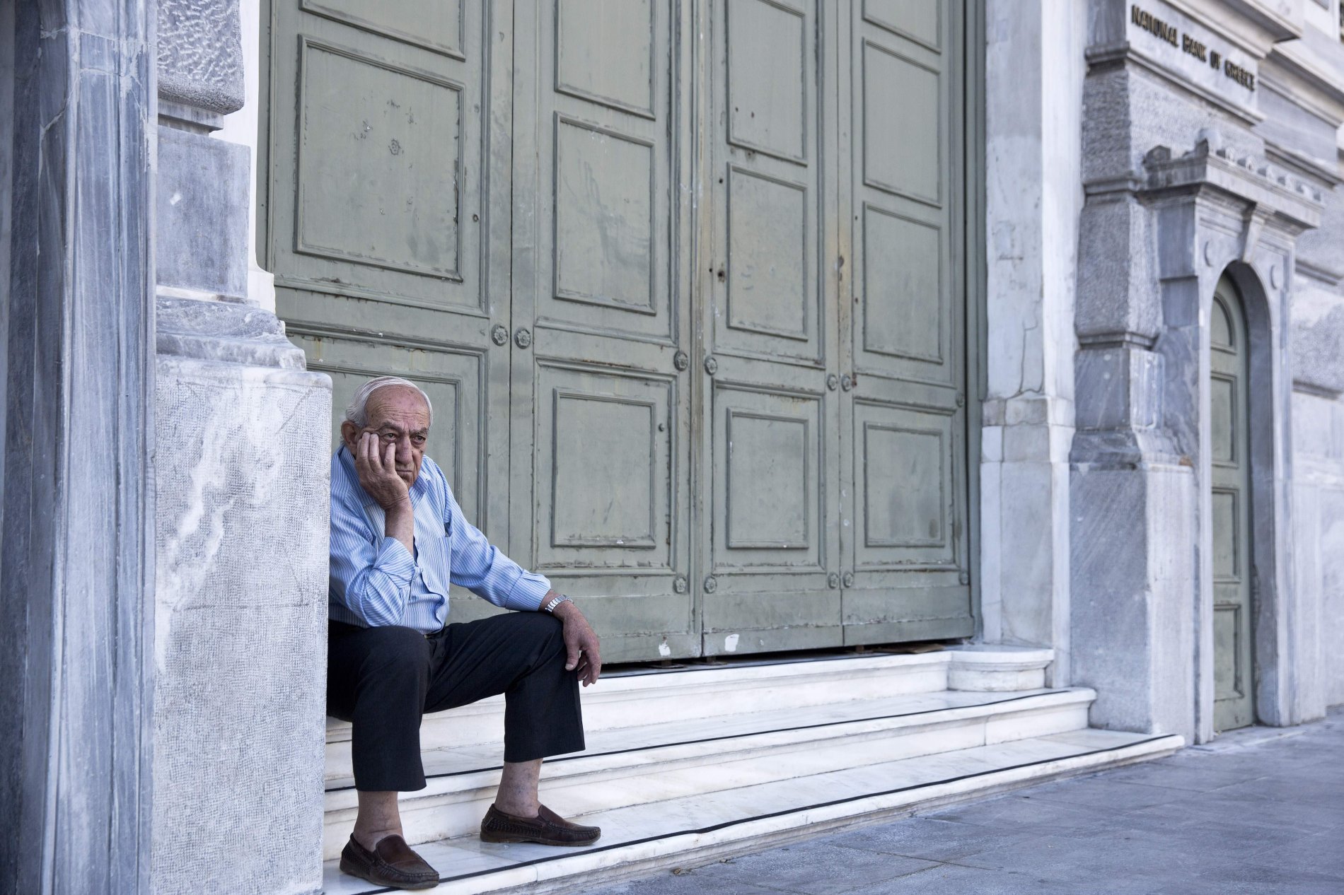 An elderly man waits to receive his pension   outside the closed too the public National bank of Greece headquarter