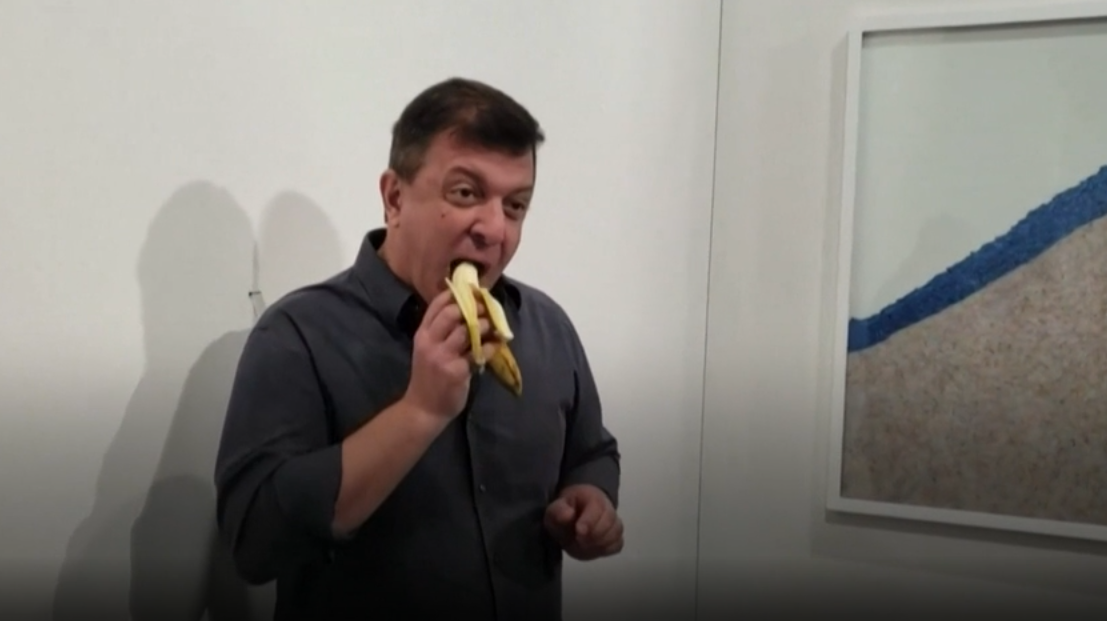 Hladový umělec David Datuna pojídá dílo jiného umělce Maurizia Cattelana