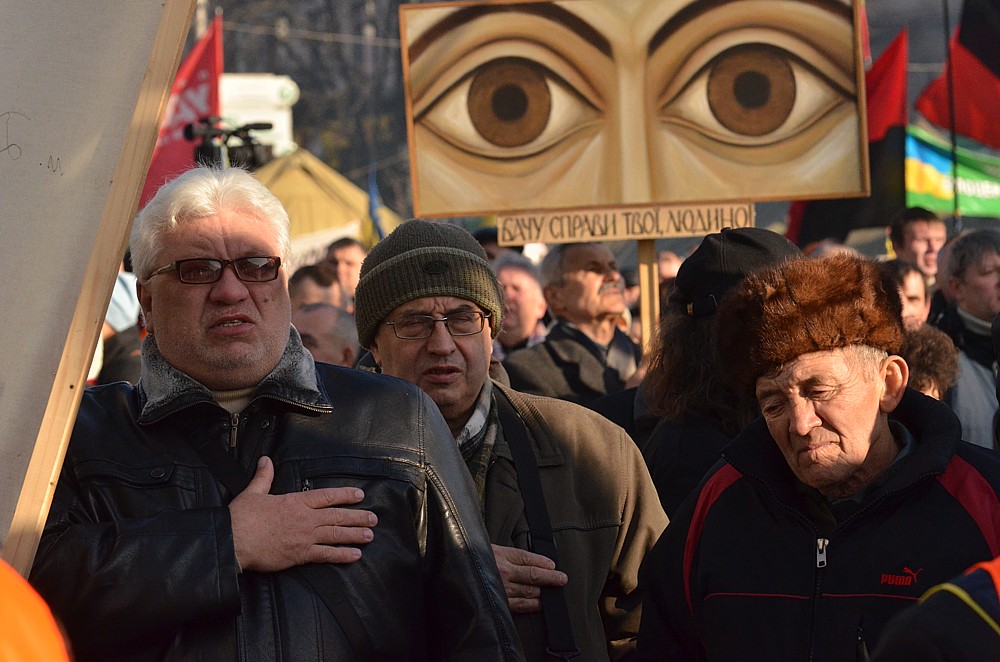 Zpěv hymny vždy doprovází ruce na srdcích demonstrantů. V pozadí oči, které jak hlásá nápis pod nimi &bdquo;vše sledují&ldquo; &ndash; jakási narážka na všudepřítomnost tajné policie.