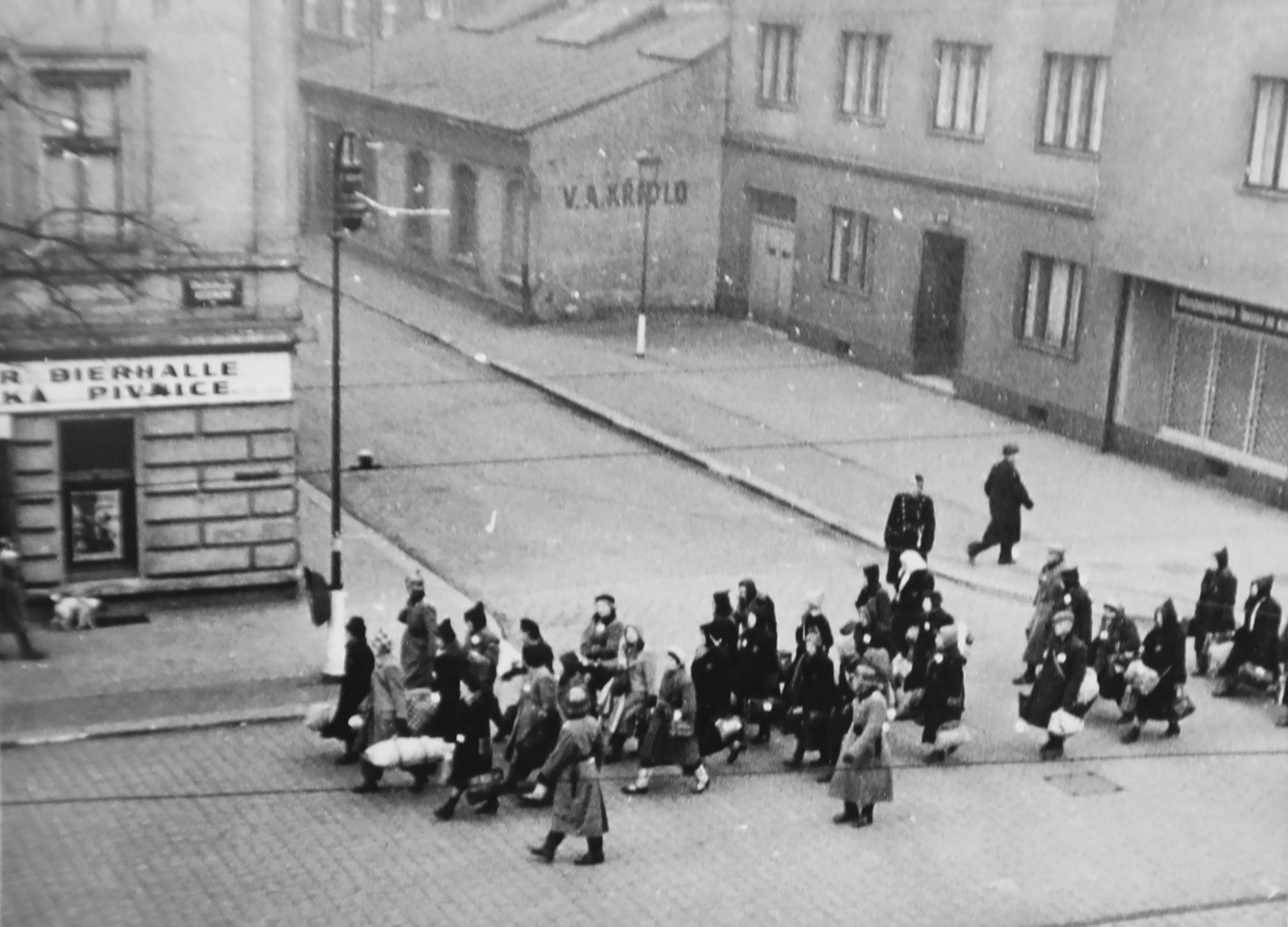 Vojáci wehrmachtu vedou židovské rodiny ranní Prahou na nádraží v Bubnech. Scéna se odehrává na rohu ulic Veletržní a U Smaltovny.
